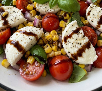 Ciotola colorata di insalata estiva con pomodorini, farro, cetrioli e foglie di basilico fresco, fotografata su tavolo di legno chiaro
