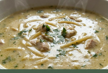 Ciotola di zuppa cremosa di pollo alle erbe con spaghetti spezzati, vapore visibile, sfondo rustico in legno